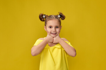 funny little child girl having fun on yellow studio background. kid holding finger on lips