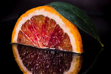 Red sicilian orange fruit cut on two and green leaf on black reflective background. Fresh, ripe bloody orange wallpaper