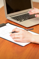 Female hands holding pen under the document and working with laptop at the table in an office