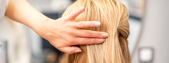 Fototapeta premium Close up of female hairdresser styling blonde hair of a young woman in a beauty salon