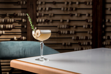 Yellow cocktail with white foam and thyme in margarita glass on the table at restaurant