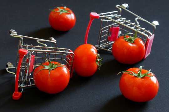 Upside-down supermarket carts and fresh red tomatoes are scattered on a dark background. Concept of trade problems, farm strikes and anti-globalization