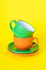 Two colorful empty tea cups and saucers. Typesetting dishes, a collection of coffee cups, a set of mugs. Ceramic painted utensils on a yellow background.