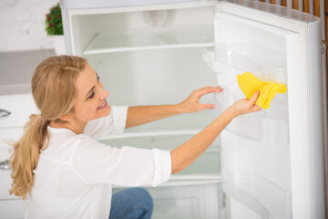 Blonde housewife in white shirt cleaning the fridge