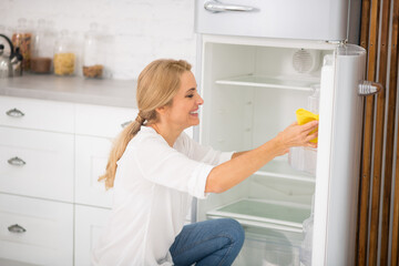 Pretty blonde housewife in white shirt cleaning the fridge and smiling