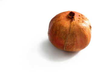 A ripe pomegranate of a small shape lies alone on a white background
