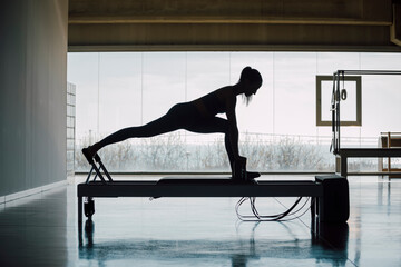 Young woman doing pilates exercises with a reformer bed. Beautiful slim fitness trainer on reformer...