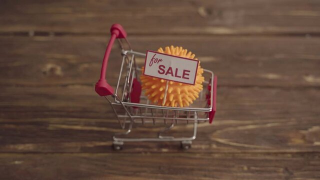 Small shopping cart with coronavirus shaped ball on table. COVID-19