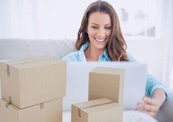Composition of cardboard boxes with smiling woman using laptop at home