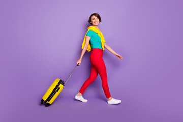 Fototapeta na wymiar Full length photo of girl walk with baggage wear knotted pullover t-shirt trousers sneakers isolated purple color background