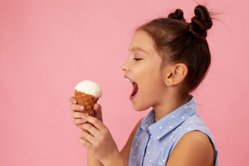 cute smiling little girl eating vanilla ice cream in a waffle cone on pink background.