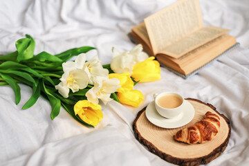 Breakfast in bed. A bouquet of tulips lies on the bed next to a cup of hot coffee. Spring. Gift. Good morning.