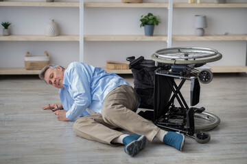 Impaired senior man lying on floor after his wheelchair tripped over indoors