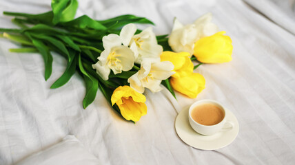 Fototapeta na wymiar Breakfast in bed. A bouquet of tulips lies on the bed next to a cup of hot coffee. Spring. Gift. Good morning.