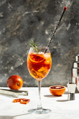 Aperol spritz cocktail in glass with fresh bloody oranges, red bitter, dry white wine, soda and ice on gray background