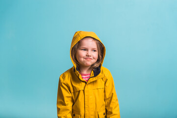Funny kid portrait against blue background. Kid girl is wearing yellow waterproof raincoat and rubber boots. Weather forecast concept