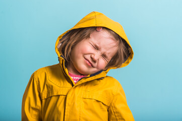 Portrait of funny kid against blue background. Kid girl is wearing yellow waterproof raincoat and rubber boots. Weather forecast concept