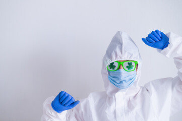 A woman in a protective suit and a medical mask and wearing funny glasses celebrates st patrick's...