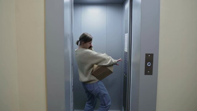 Young woman enters in the elevator with cardboard boxes and folding chair moving in to new appartment