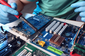Technician repairing electronic circuit board with soldering iron at table, closeup