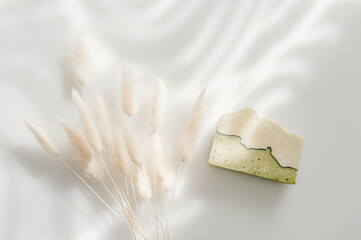 Handmade soap and dried bunny tail grass. Sunshade shadow on white background. Zero waste, eco friendly cosmetics concept. Vintage color filter.