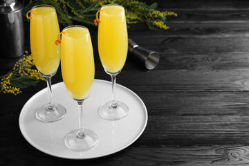 Glasses of Mimosa cocktail with garnish on dark wooden table. Space for text