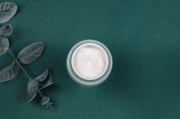 Top view of an open jar of cream and green leaves on a colored background. Beauty concept with cosmetic products for the face.