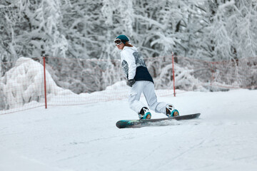 cheerful woman riding on snowboard in the mountains in winter. woman in white ski suit
