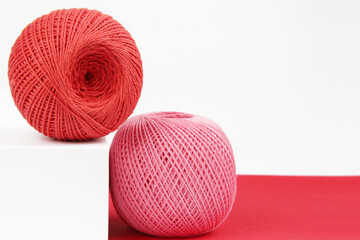 Crimson and pink balls of cotton crochet thread on a geometric red and white background. The concept of your favorite hobby of needlework, online knitting courses. Copyspace.