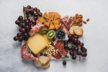 Cheese, slicing salami, ham, grapes, nuts and fruits on marble board. Party snacks.  Wine appetizer on white background, top view 