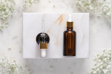 Cosmetic bottles with pipettes on marble box. Marble background with white gypsophila flowers....
