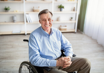 Portrait of joyful impaired senior man in wheelchair posing and smiling at home