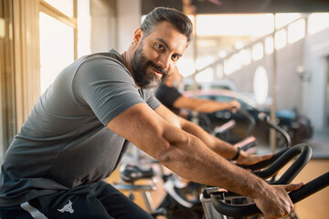 Plakat Portrait of a Young athletic man in sportswear doing cycling on exercise bikes at the gym