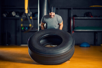 Naklejka na ściany i meble Muscular man working out in gym flipping a tire 