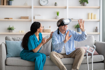 Disabled senior man using VR headset with young nurse, exploring augmented reality at home