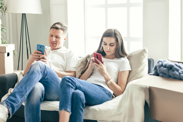 young couple with smartphones sitting on the sofa in a new apartment .