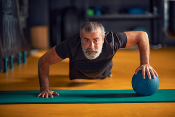 Strong and healthy middle-aged man doing push-ups with a ball
