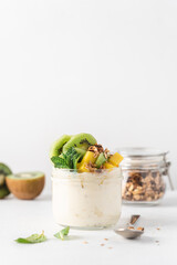 Mango yogurt with granola and kiwi in glass jar on white background. Healthy breakfast. Side view, close up
