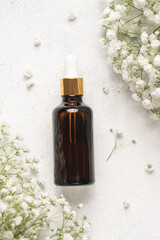 Cosmetic glass bottle with dark glass pipette on light background with gypsophila flowers. Natural cosmetics concept