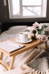 Coffee table on bed. Flowers, cup, candles, note pad, pen. Gray interior, plaid