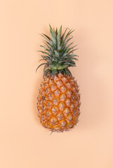 Top view of fresh pineapple with tropical leaves on pastel orange background.