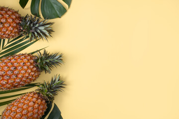 Top view of fresh pineapple with tropical leaves on yellow background.