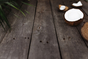 Broken coconuts on gray wooden background with palm leaf. White coconut pulp