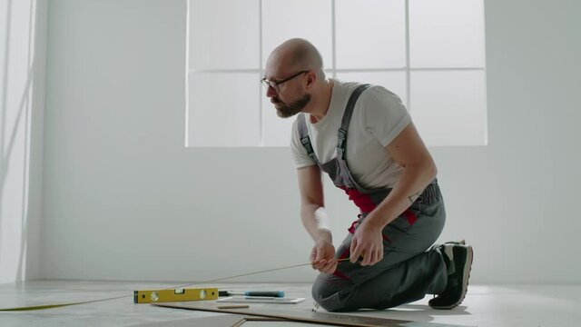 Laborer with glasses measures parquet with retractable tape