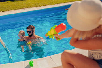 Parents and child playing with squirt guns at the swimming pool