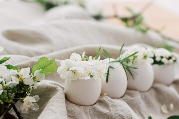 Happy Easter! Natural eggs in floral wreaths on linen fabric with blooming spring branch and petals
