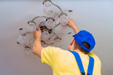 Electrician screws a chandelier to the ceiling close-up