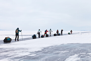 A group of tourists ice skating with ski poles, tents and backpacks travels on the ice of the frozen Lake Baikal to Olkhon Island on a cold winter day. Active holidays