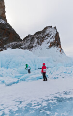 Frozen Lake Baikal. The famous Cape Hoboy on Olkhon Island in winter attracts tourists with beautiful icy rocks. Tourists girls inspecting the blue ice hummocks. Winter travel and active  holidays