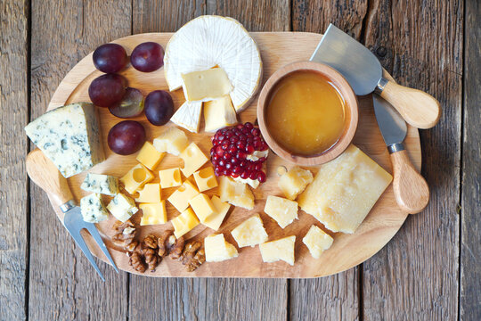 Cheese board with camembert cheese, parmesan cheese, maasdam cheese. The composition is complemented by honey in a wooden plate, grapes and walnuts. Special knives are nearby. Top view.